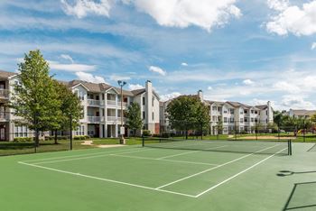 A tennis court is surrounded by apartment buildings.